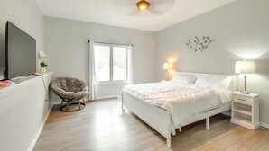 Ein Schlafzimmer mit Bett, Nachttischen, einem Sessel, einem Fernseher und einem Fenster.