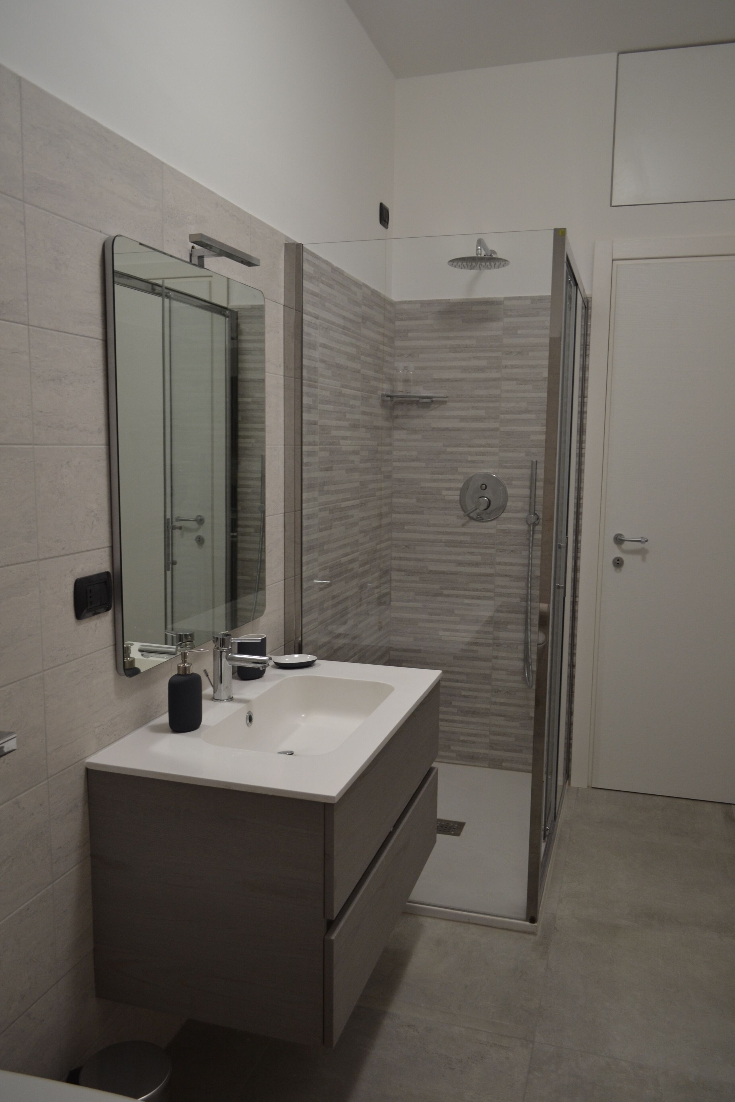 Uma casa de banho moderna com um espelho grande, uma pia, um chuveiro e sanita.