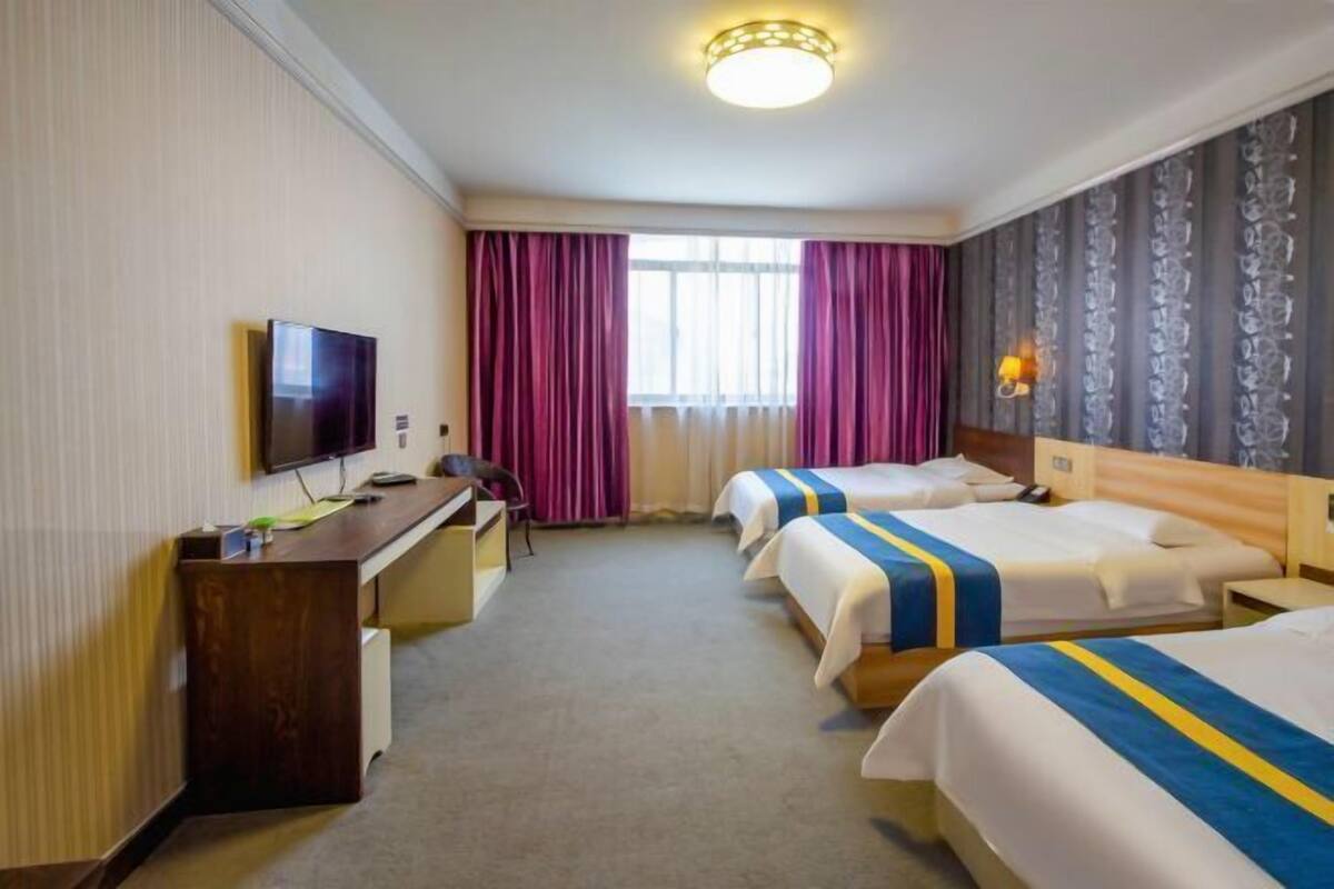 A hotel room with two beds, a desk, a television, and a window with curtains.
