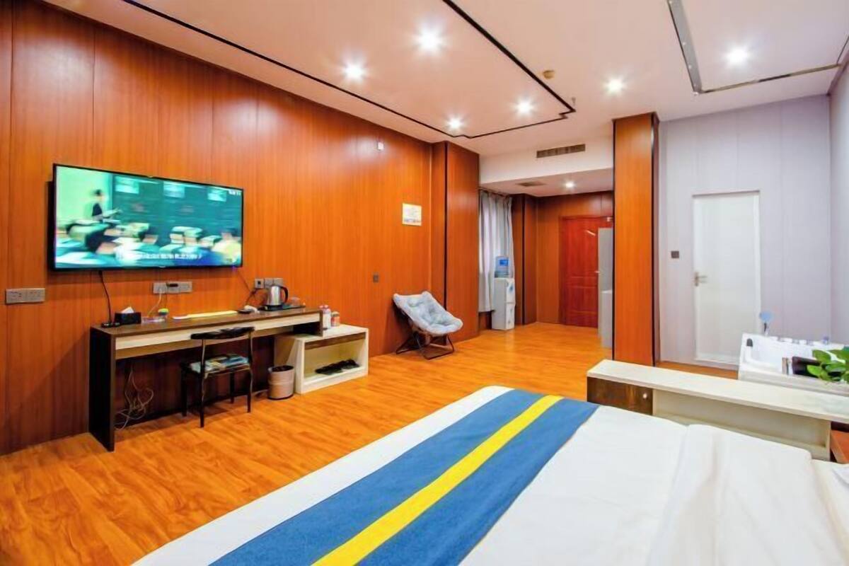 Ein Hotelzimmer mit Holzboden, einem Bett mit blau-gelb gestreifter Bettdecke, einem Schreibtisch mit Fernseher und einem Sessel.