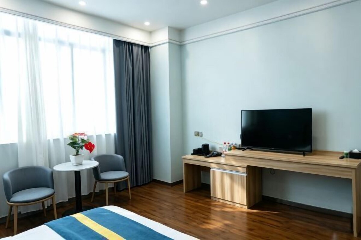 A hotel room with a bed, a desk, a television, and a window with curtains.