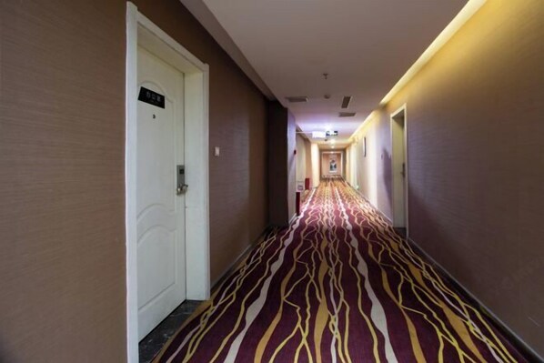 Un couloir d’hôtel avec un tapis à motifs, des portes blanches et un panneau sur le mur.