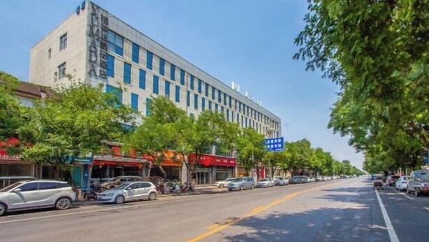 A street view with a modern building, parked cars, and trees lining the road. - Yumeida Boutique Hotel Xinxiang Changheng (Changyuan)