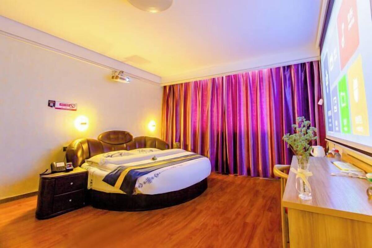 Ein Hotelzimmer mit Bett, Nachttischen, Schreibtisch und einem großen Fenster mit Vorhängen.