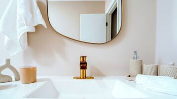 Un bagno con un lavandino bianco, un rubinetto dorato, uno specchio rotondo, un asciugamano bianco e una candela.