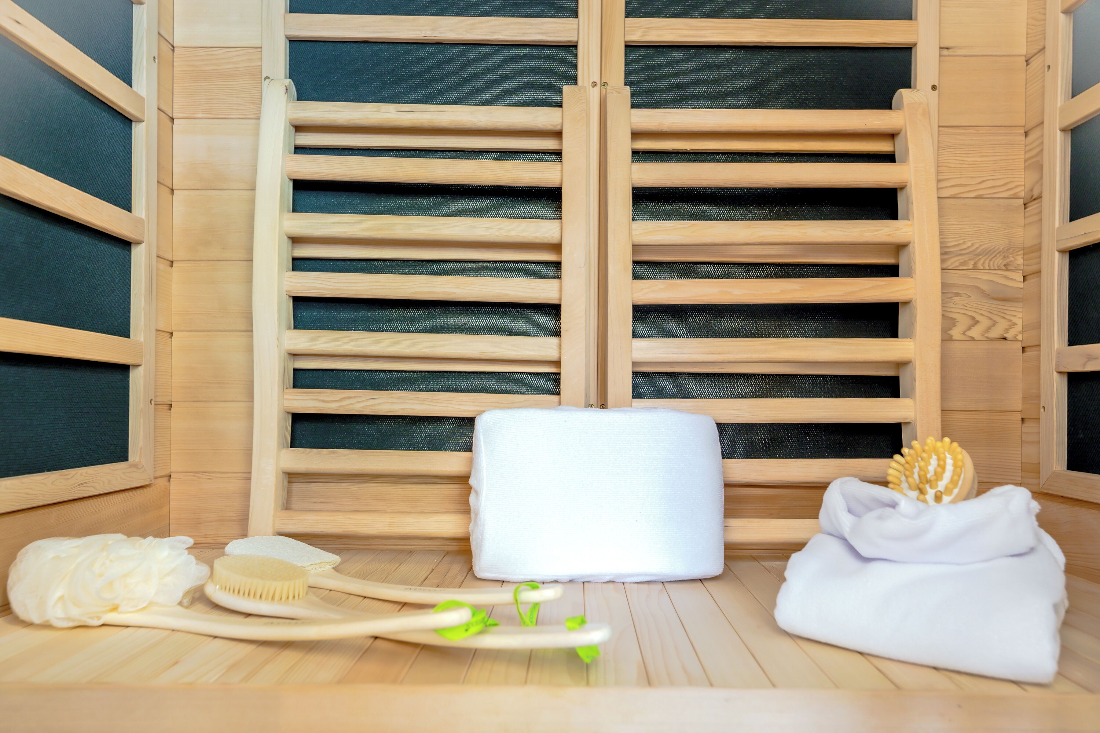 A wooden sauna room with a bench, towels, a brush, and a bottle.