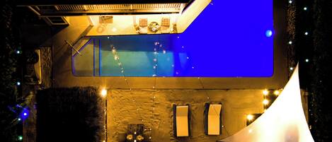 A modern house with a large swimming pool, outdoor seating, and string lights.