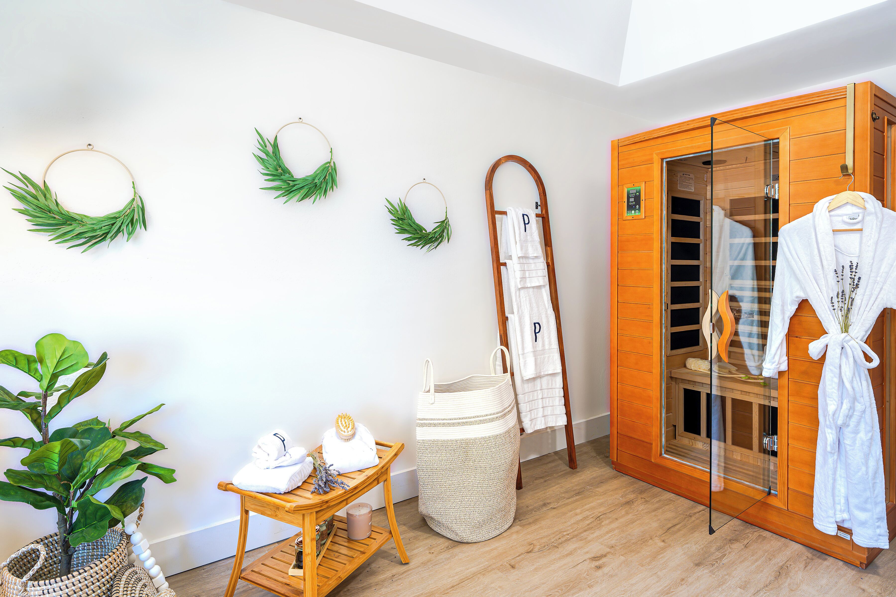 Une salle de spa avec un sauna en bois, un banc en bois, une plante, une petite table avec des serviettes et un peignoir suspendu.