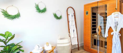 Une salle de spa avec un sauna en bois, un banc en bois, une plante, une petite table avec des serviettes et un peignoir suspendu.