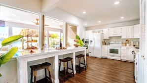 Una cocina amplia con armarios blancos, una isla grande con taburetes y vistas al exterior.