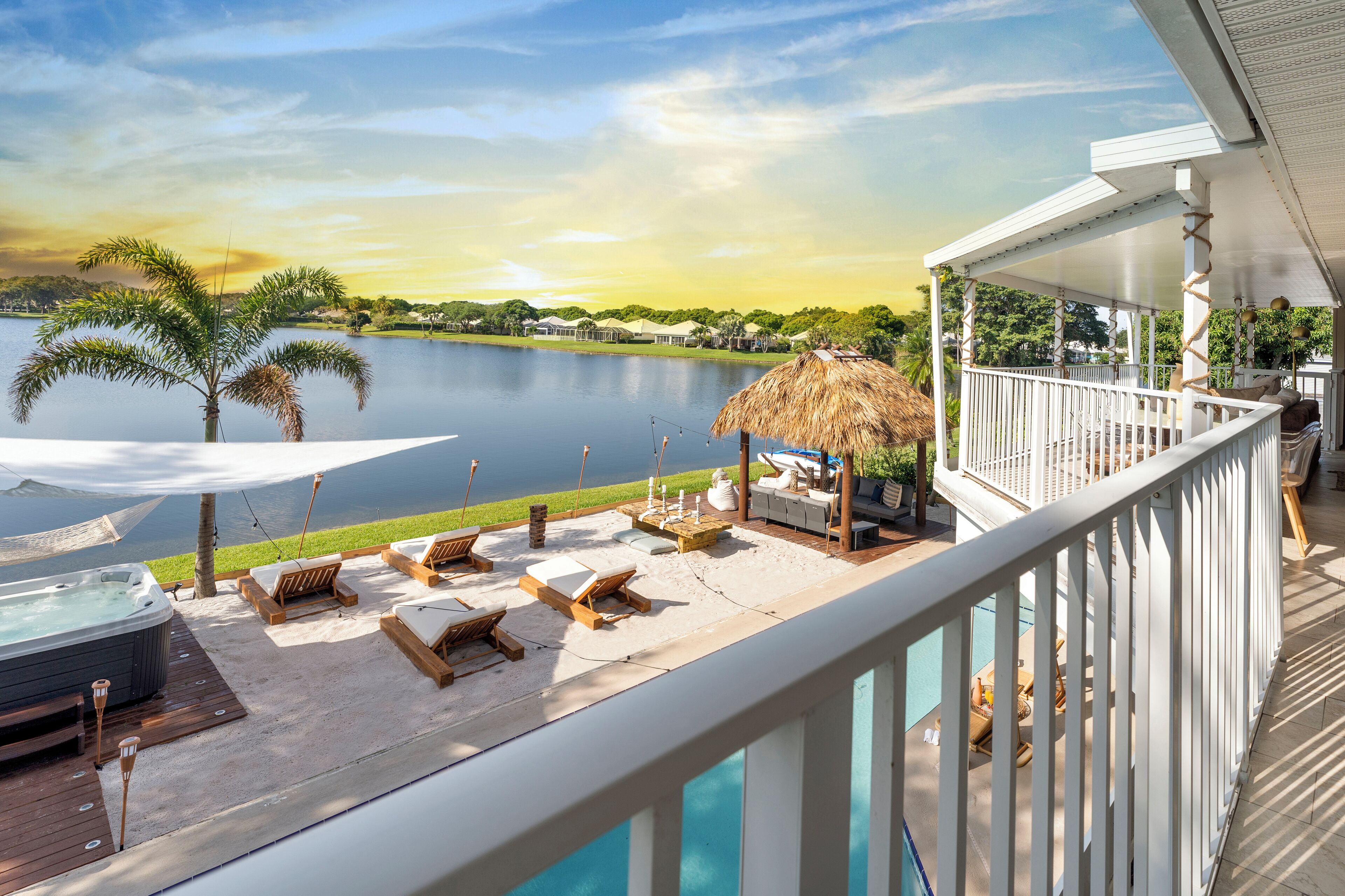 A deck with lounge chairs, a hot tub, and a view of a lake and mountains.