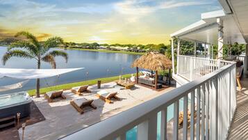A deck with lounge chairs, a hot tub, and a view of a lake and mountains.