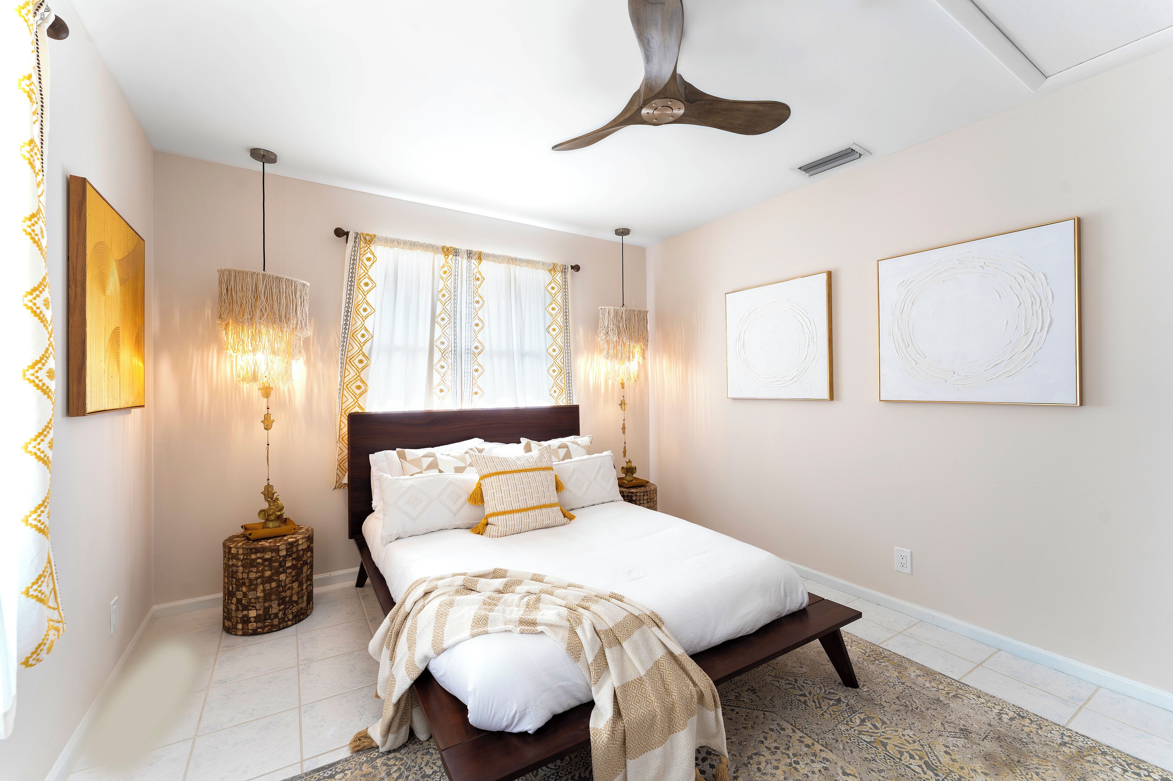 A bedroom with a bed, bedside lamps, a ceiling fan, and artwork on the walls.