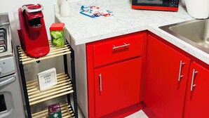A kitchen with red cabinets, a microwave, a coffee maker, and a shelf with kitchen items.