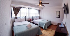Habitación de hotel con dos camas, ventilador de techo, televisión y ventana con cortinas.