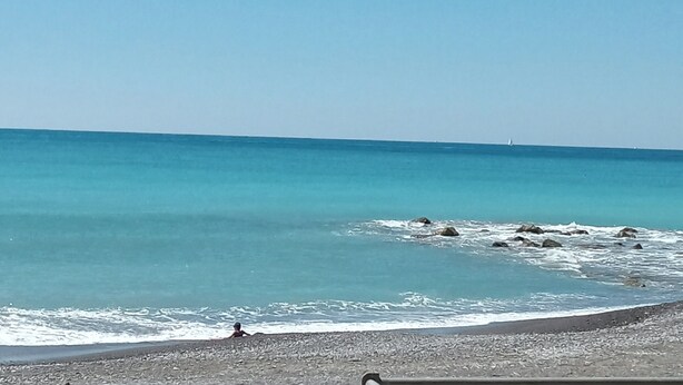 A beach with clear blue water and a person in the water.