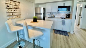 Eine moderne Küche mit weißen Schränken, einem Edelstahl-Kühlschrank, einer Mikrowelle und einer Bar mit weißen Hocker.