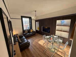 Una sala de estar moderna con un sofá de cuero, una mesa de comedor de vidrio y un televisor montado en la pared.