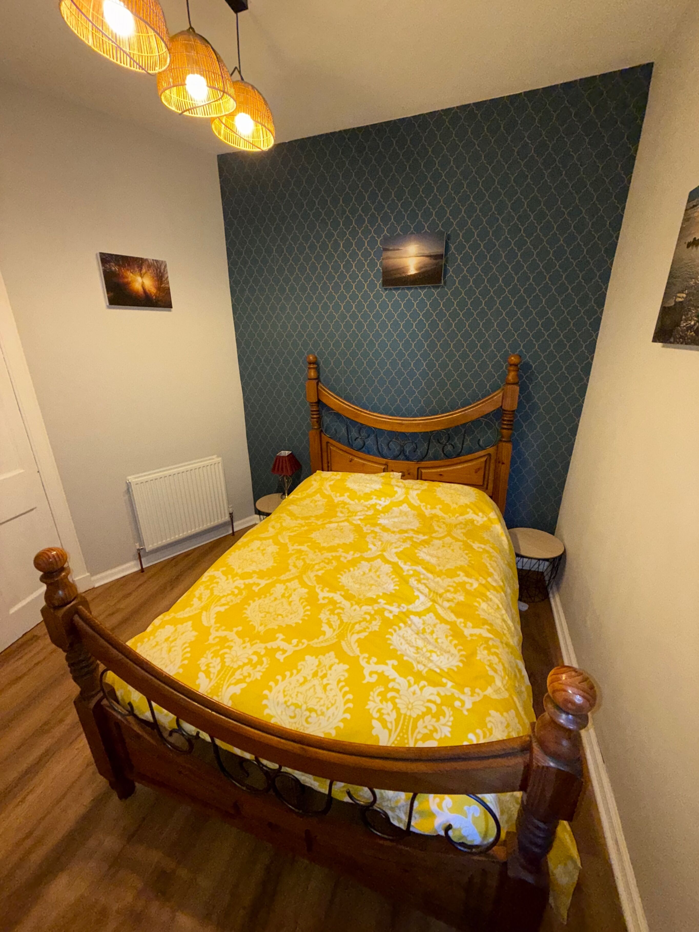 Ein Schlafzimmer mit einem hölzernen Bett, einer Wand mit blauem Muster und einer gelben Tagesdecke.