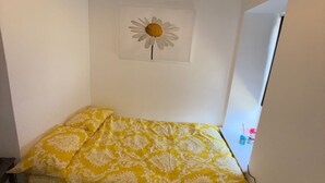 A small, single-bed room with a yellow patterned bedspread, a white wall, and a framed picture of a daisy. - Ayr Town Centre Apartment - 3 Bedrooms (Ayr)