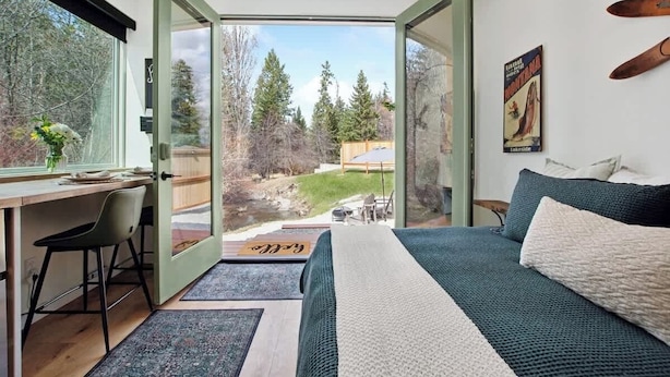 A bedroom with a large bed, a desk, and a view of a backyard. - Peaceful Creekside Villa, Walk to Flathead Lake (Lakeside)