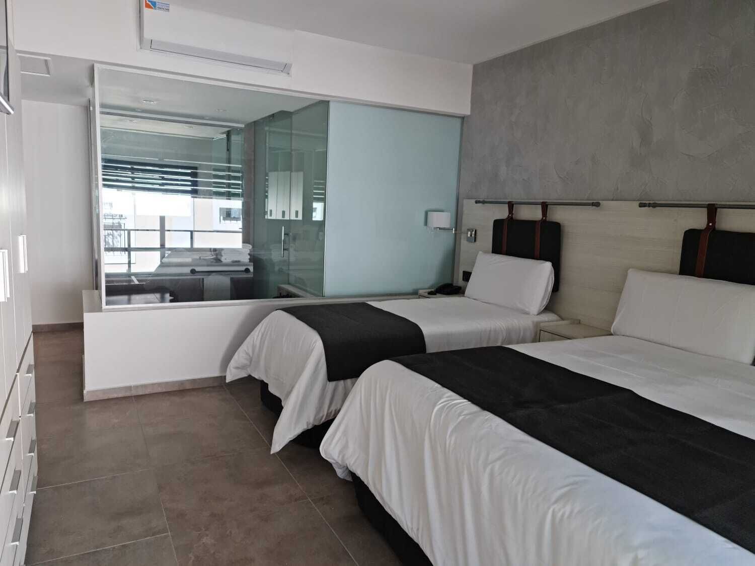 Habitación de hotel con dos camas, un espejo grande y vista al exterior.