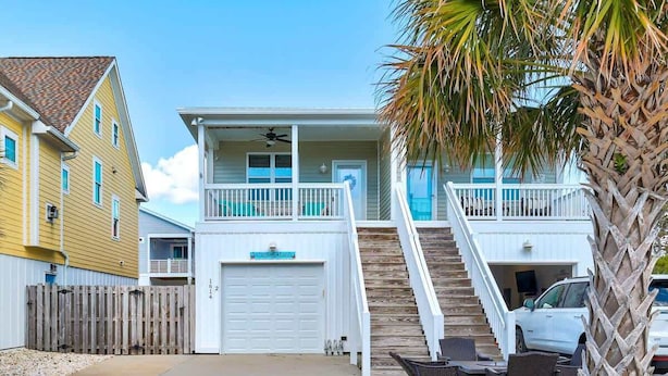 A two-story beachfront house with a white exterior, a balcony, and a staircase leading to the garage. - Butterfly Oasis (Carolina Beach)