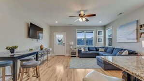 A modern kitchen with a dining area, a living room with a sofa, and a ceiling fan. - Butterfly Oasis (Carolina Beach)