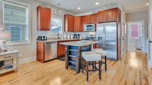 A modern kitchen with wooden cabinets, stainless steel appliances, and a central island with bar stools. - Butterfly Oasis (Carolina Beach)
