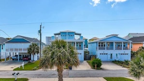 A residential area with houses featuring a central blue building with a garage, surrounded by other houses and palm trees. - Butterfly Oasis (Carolina Beach)