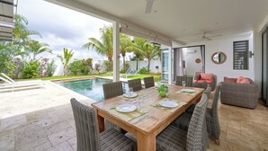 Ein großzügiger Außenbereich zum Essen mit Pool, Korbmöbeln und Blick auf den Garten.