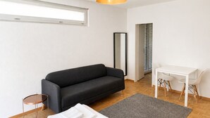 A modern room with a sofa, a small round table, a white desk with chairs, a grey rug, and a large mirror. - Fantastic studio in the city centre (Art 8) (Zürich)