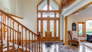 A grand entrance with a wooden staircase, a glass door with an exit sign, and a marble floor.