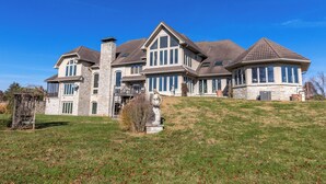 A large, multi-story house with a stone facade, multiple windows, and a prominent chimney.
