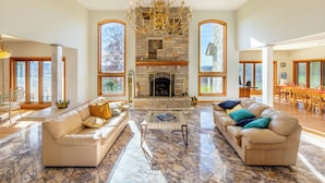 A spacious living room with a stone fireplace, leather sofas, and a chandelier.
