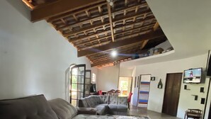 A spacious living area with a large sectional sofa, a patterned rug, and a wooden ceiling. - Nature, swimming pool, billiards, barbecue and comfort – Quinta do Remanso (Mairiporã)