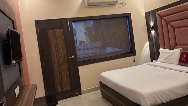 A bedroom with a bed, a window, an air conditioning unit, a TV, and a bedside table. - DM PAYING GUEST HOUSE (VARANASI)