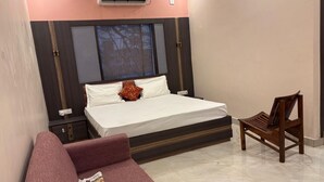 A bedroom with a bed, a wooden chair, and a red sofa. - DM PAYING GUEST HOUSE (VARANASI)