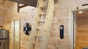 A wooden interior with a wooden staircase, a fan, and a door with a sign.