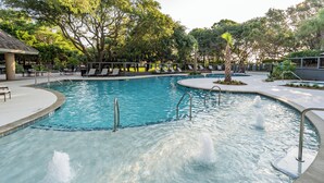 Ein Pool mit gewölbter Kante, umgeben von Liegestühlen und einer überdachten Sitzecke.