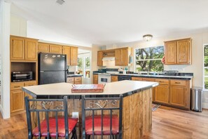 A kitchen with wooden cabinets, a black refrigerator, a microwave, and a dining area with red chairs.