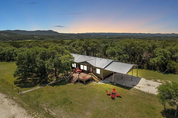 A single-story house with a covered patio, surrounded by trees and a hilly landscape.