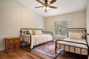 A bedroom with two metal beds, a wooden nightstand, a patterned rug, and a ceiling fan.