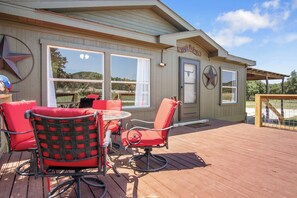 A covered outdoor seating area with a table and chairs, a door with a window, and a sign that reads 'Welcome'.