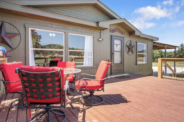 A covered outdoor seating area with a table and chairs, a door with a window, and a sign that reads 'Welcome'.