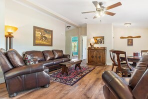 A spacious living room with leather sofas, a wooden coffee table, and a dining area with a wooden table and chairs.