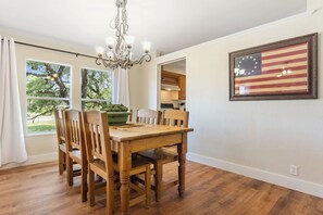 Ein Essbereich mit einem Holztisch und Stühlen, einer Kristallleuchter und einer amerikanischen Flagge im Bilderrahmen an der Wand.