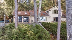 A two-story house with a sloped roof, surrounded by dense evergreen trees and a wooden deck. - Chestnut Cove Cottage- Winnipesaukee - Alton (Alton)