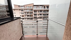En balkon med gelænder, udsigt til en høj bygning og flisegulv.