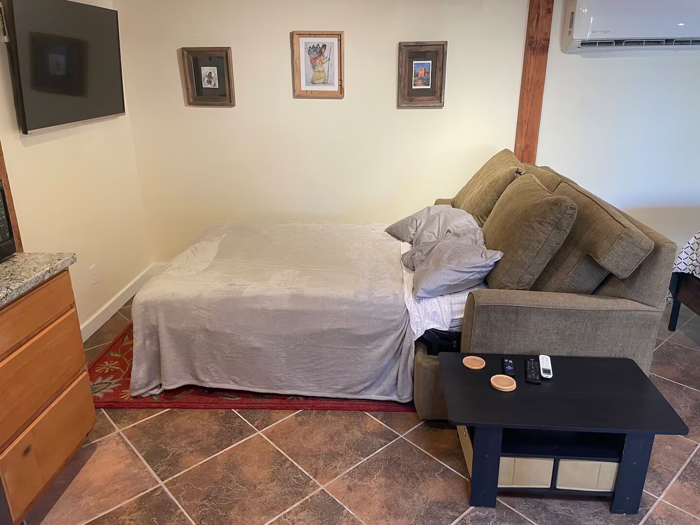 A bedroom with a bed, a couch, a small table, and a TV.